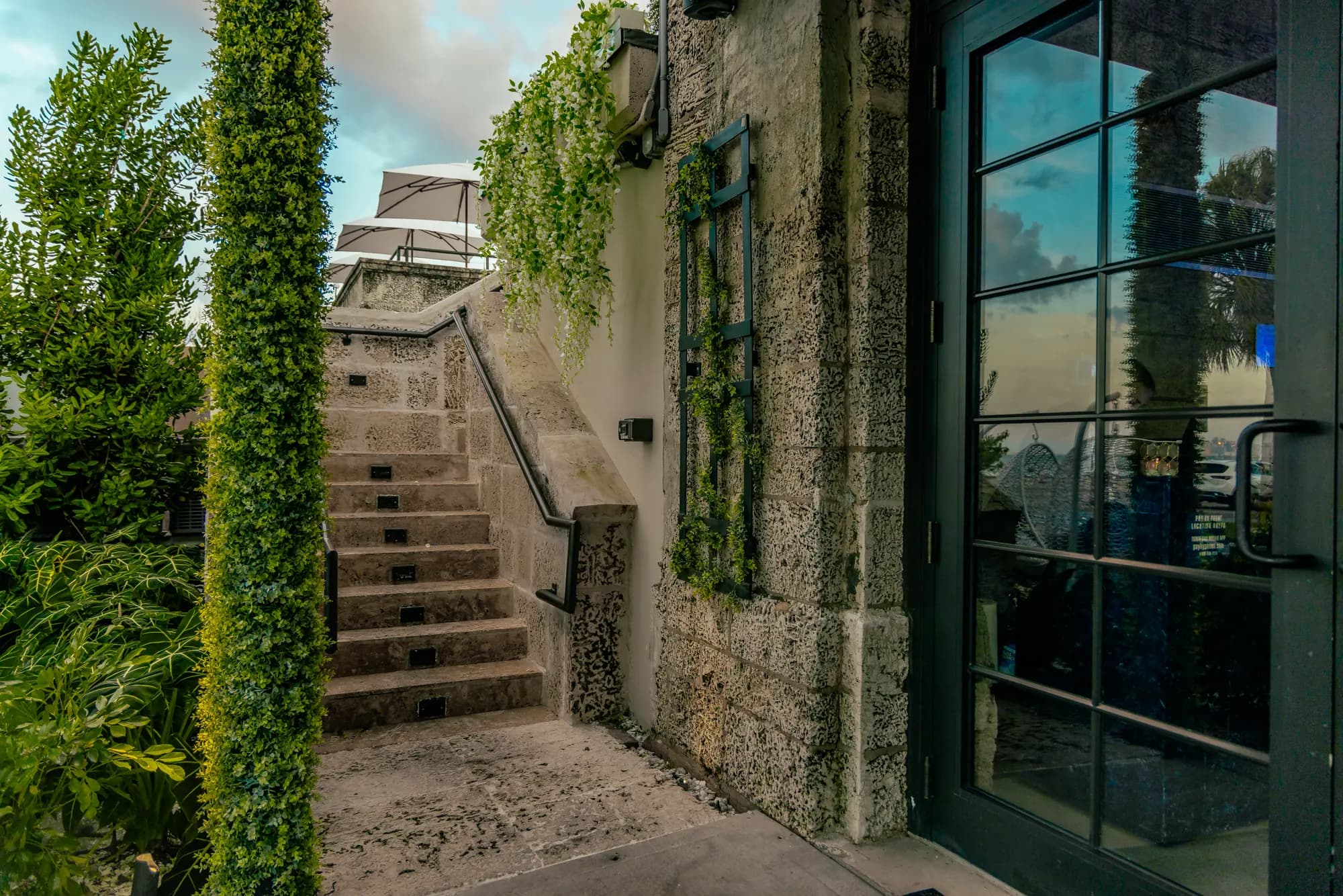 The coral-rock wall beside the entrance, a stair climbing between the ivy and the tall glass doors