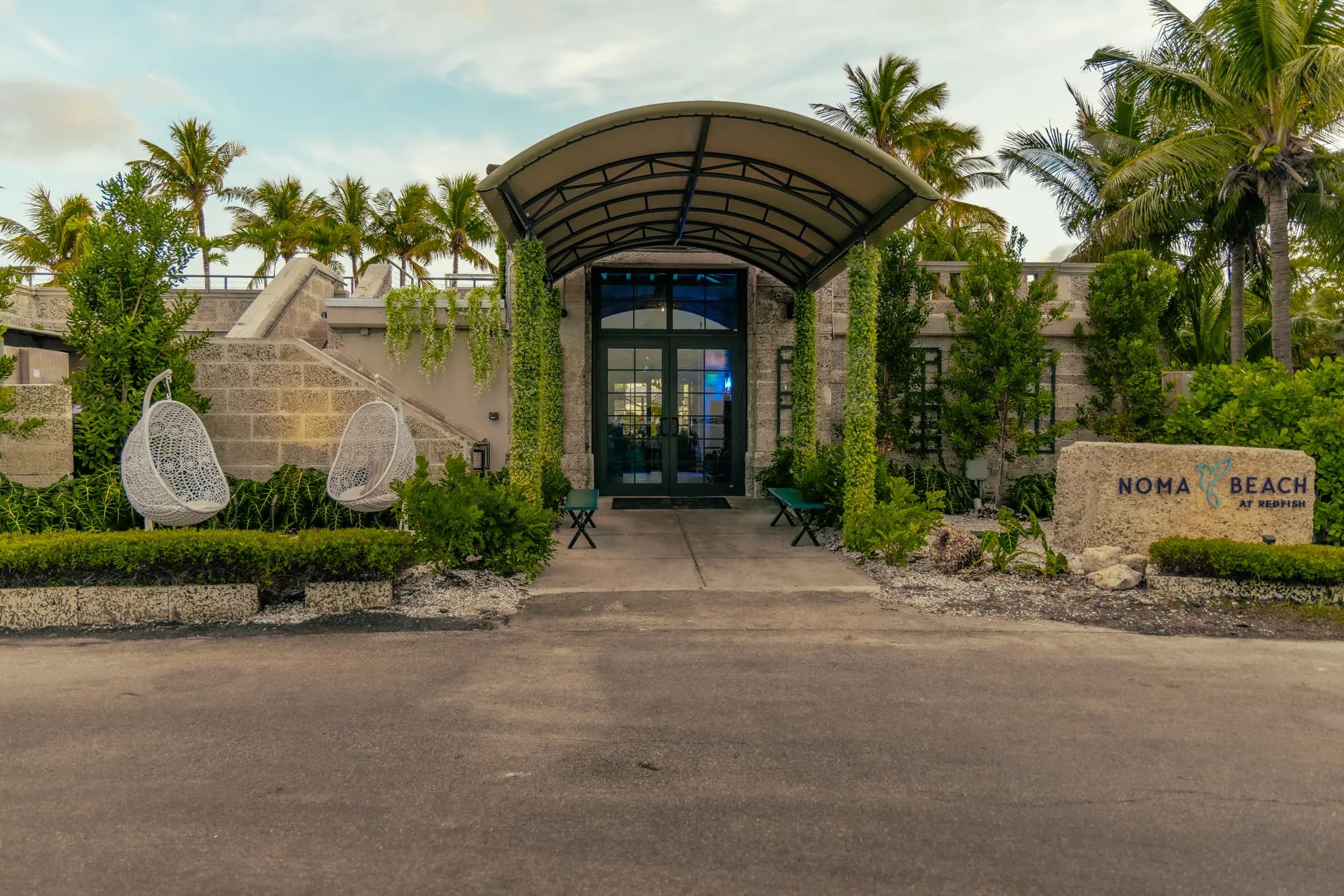 The entrance under its arched awning, ivy on the columns, two white egg chairs and the stone sign beside the door