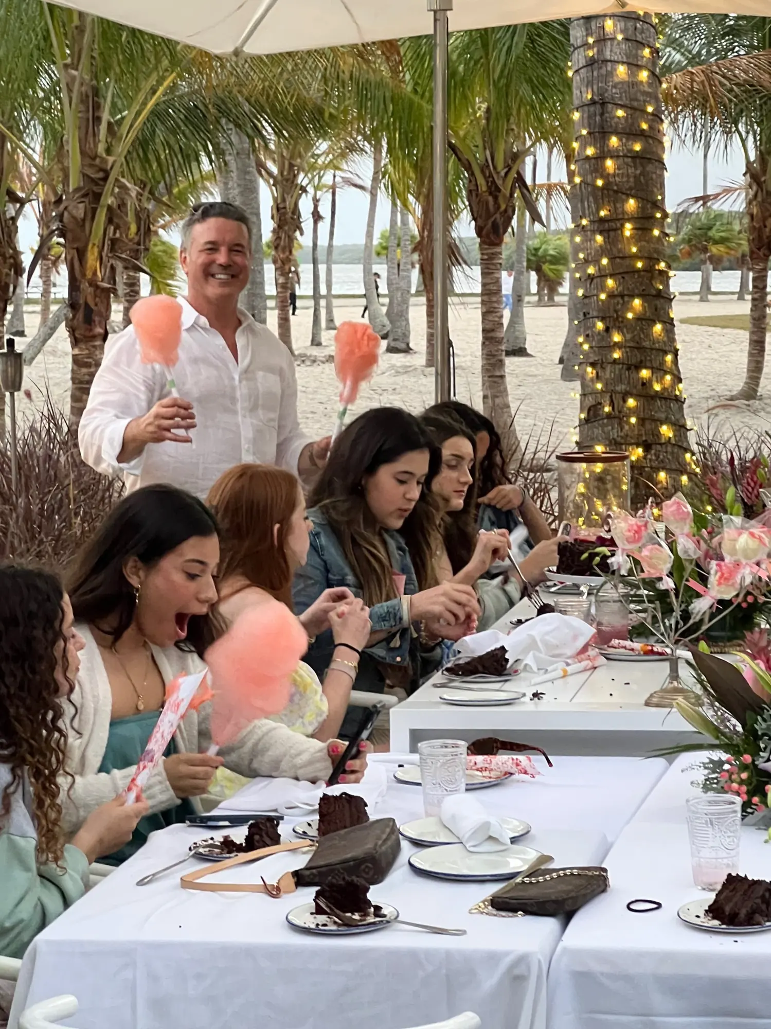 Guests laughing over cake and cotton candy at a long table on the patio