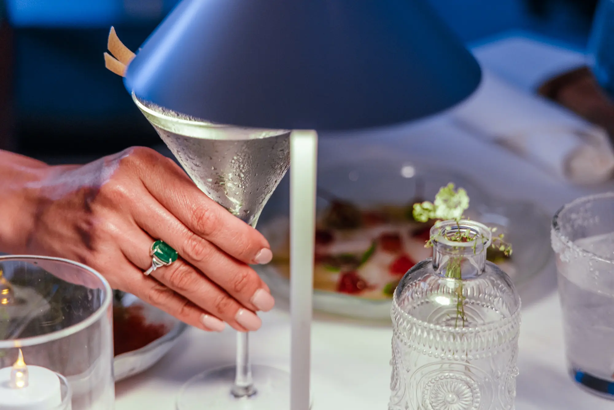 A hand lifting a martini beside the table lamp