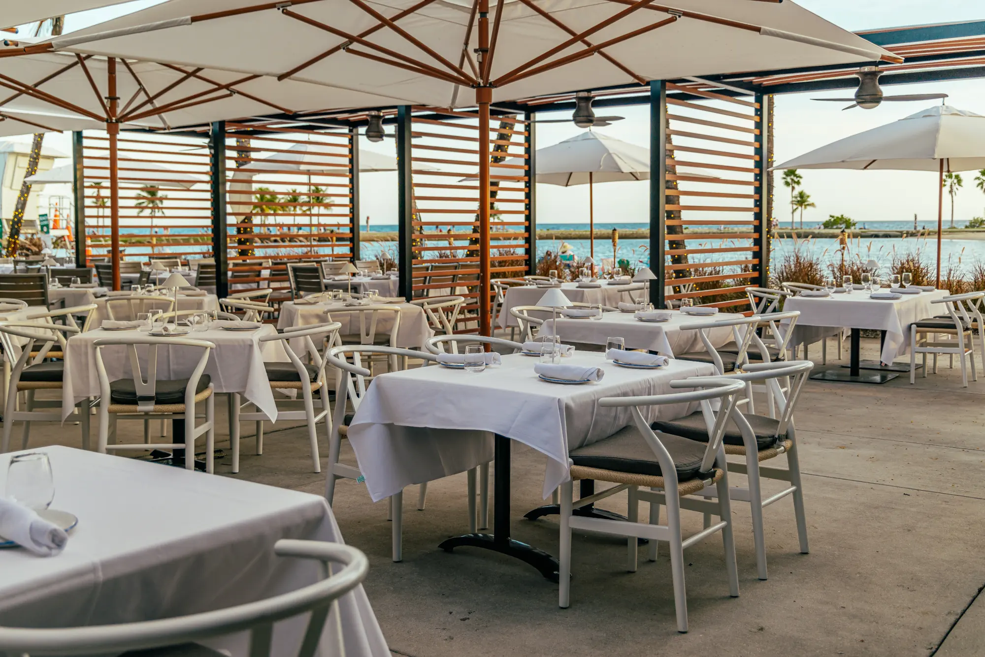 The patio under its white umbrellas, set for dinner, open to the lagoon and the bay