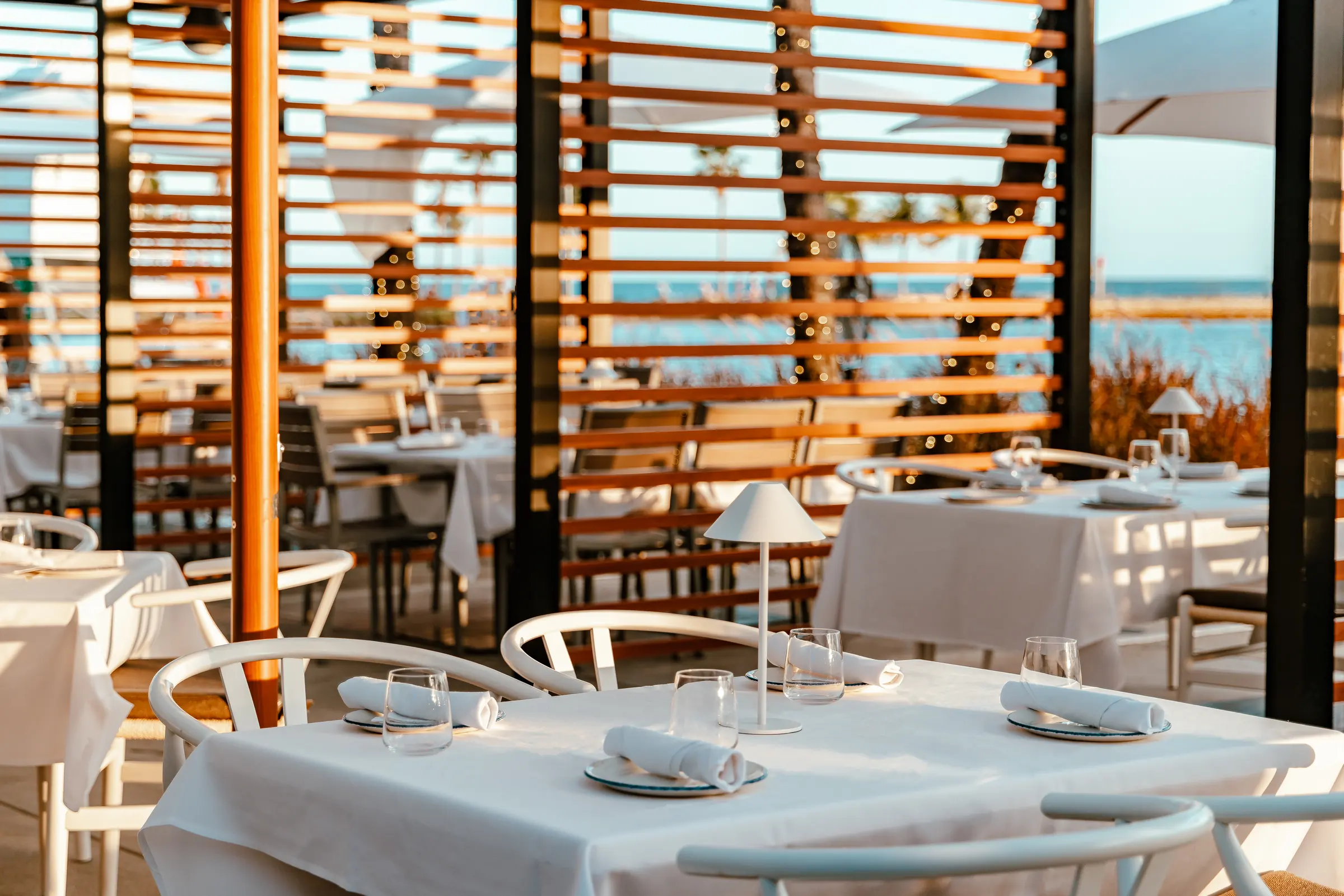 Tables set under the pergola, the lagoon and the bay beyond its slats