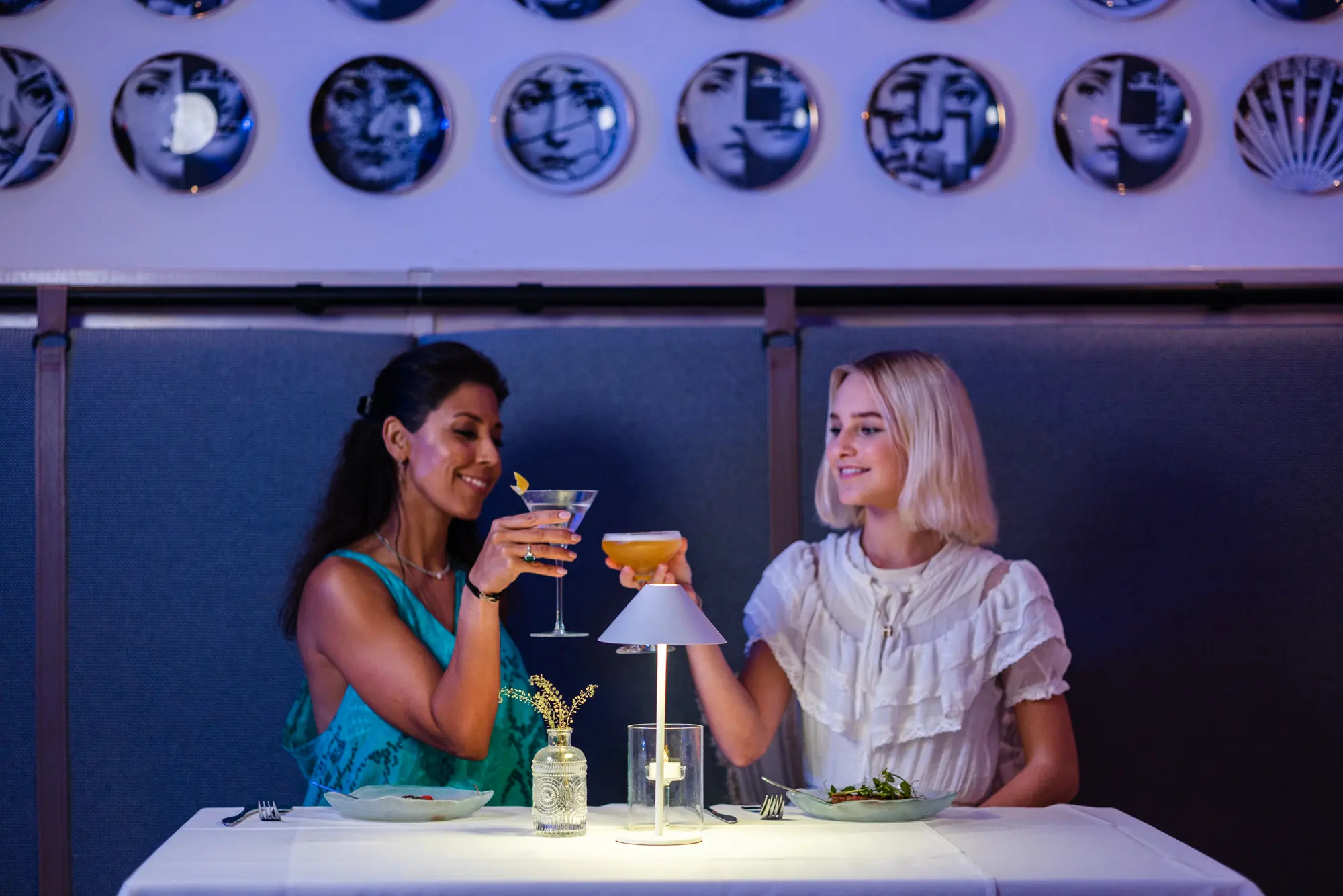 Two guests raising their cocktails under the wall of plates