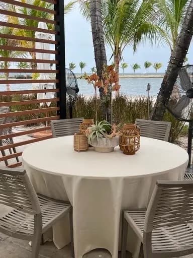 A round table in white linen set for an event, flowers and lanterns in the middle