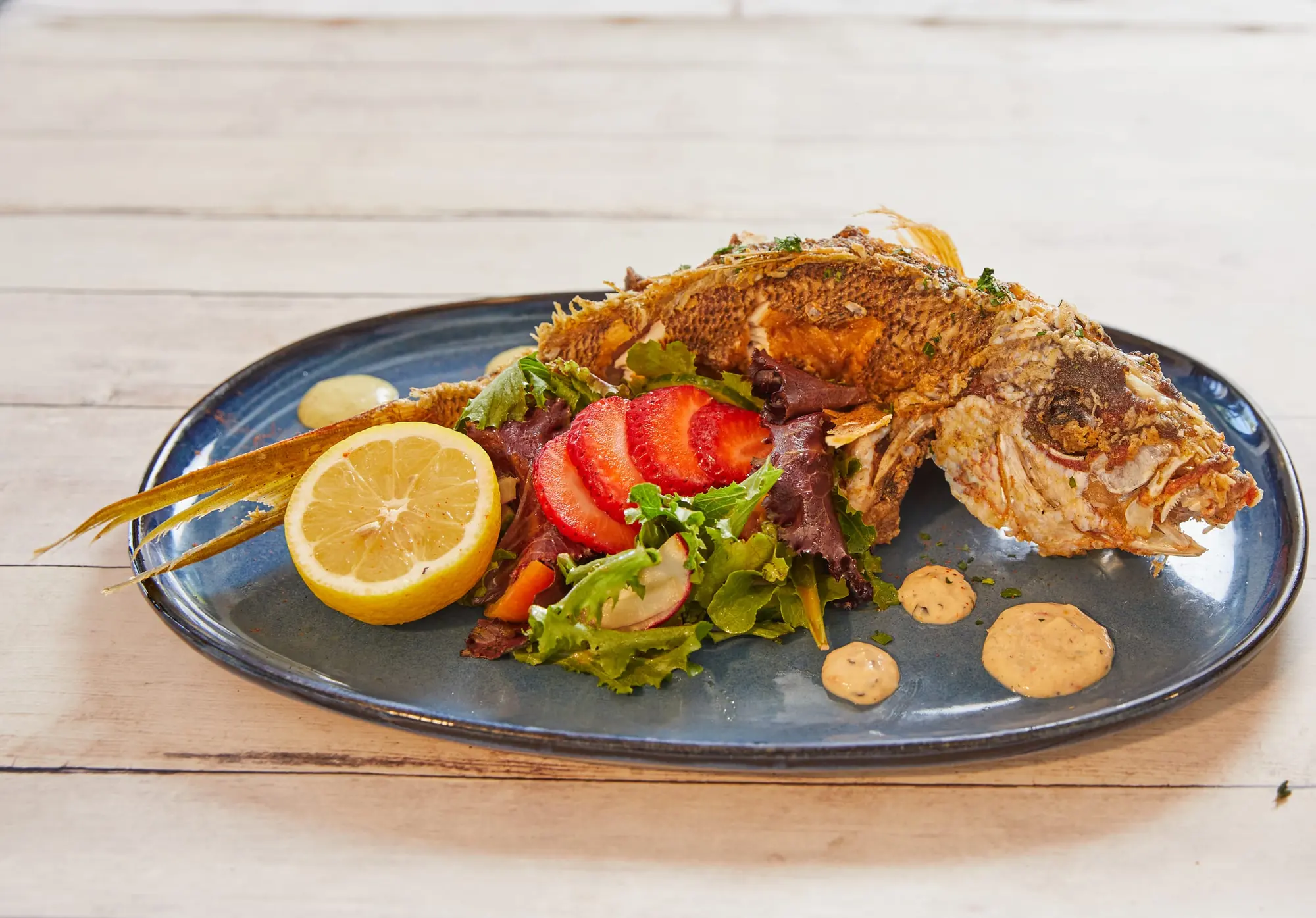 The fried whole snapper on a blue platter with lemon, tomatoes and greens